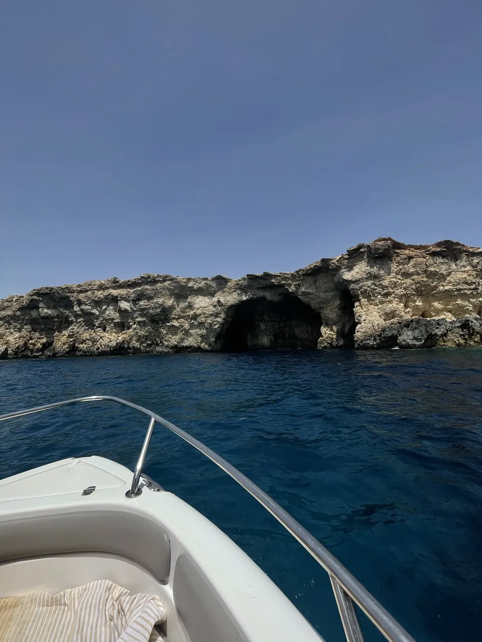 Prua di una barca a motore davanti a una costa rocciosa con una grotta scura